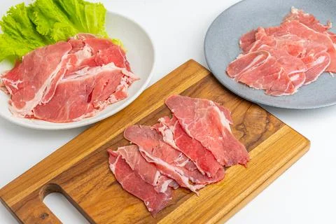 Fresh raw sliced beef meat on wooden board and plate with green lettuce iso.. Stock Photos