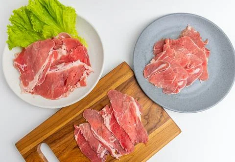 Fresh raw sliced beef meat on wooden board and plate with green lettuce iso.. Stock Photos