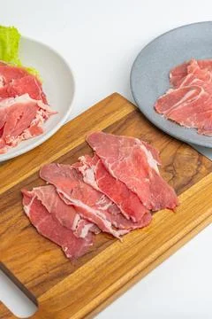 Fresh raw sliced beef meat on wooden board and plate with green lettuce iso.. Stock Photos