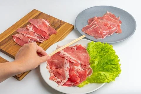 Fresh raw sliced beef meat on wooden board and plate with green lettuce iso.. Stock Photos