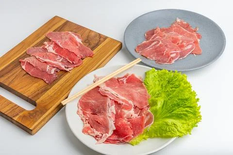 Fresh raw sliced beef meat on wooden board and plate with green lettuce iso.. Stock Photos