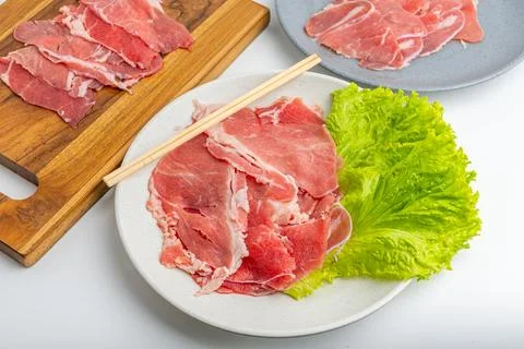 Fresh raw sliced beef meat on wooden board and plate with green lettuce iso.. Stock Photos