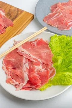 Fresh raw sliced beef meat on wooden board and plate with green lettuce iso.. Stock Photos