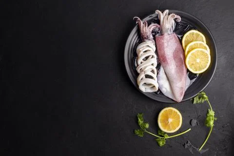Fresh raw squid. Raw squid on a black plate with ice. Lemon slices. Top vie.. Stock Photos