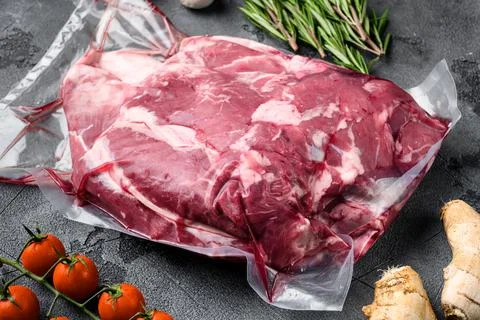 Fresh, raw, vacuum packed cut lamb meat, with ingredients and herbs, on gray Stock Photos