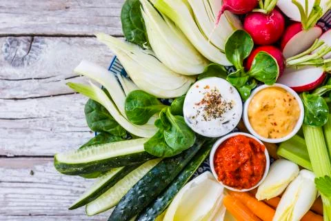 Fresh raw vegetables with different sauces on a wooden background. Stock Photos