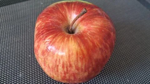 Fresh red apple with a sturdy stem on textured surface Stock Photos