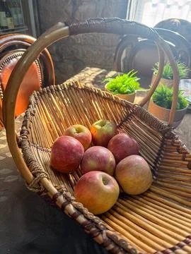 Fresh red apples in a rustic woven basket on a table, bathed in sunlight, spr Foto stock