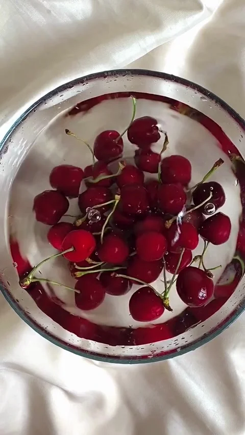 Fresh red cherries splashing into a clear bowl of water Stock Footage 344016952
