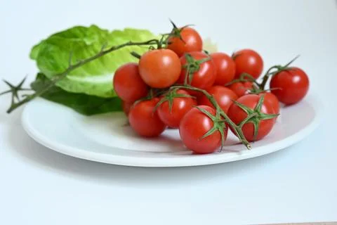Fresh red cherry tomatoes on vine with green lettuce leaf on white plate. Stock Photos