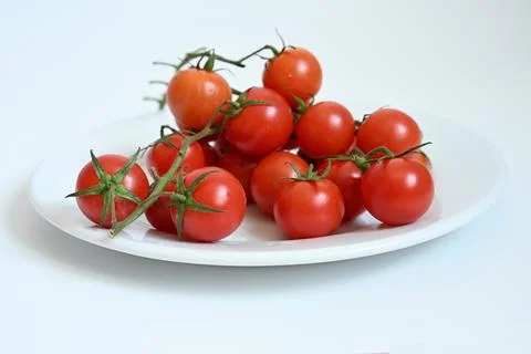 Fresh red cherry tomatoes on a vine served on a white ceramic plate. Fotos de archivo