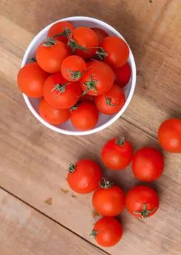 Fresh red cherry tomatoes in a white bowl and on wood table Stock Photos