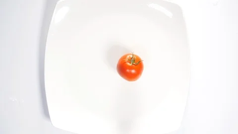 A fresh red tomato falling onto a white plate into a water splash, close up Stock Footage 88507747