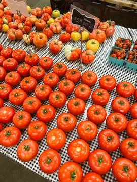 Fresh red tomatoes displayed on checkered tablecloth at local market during Stock Photos