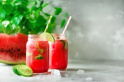 Fresh red watermelon slice and smoothie in glass jar with straw, ice, mint, lime Stock Photos