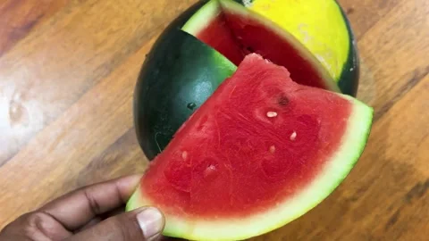 Fresh red watermelon slice held by hand with ripe watermelon on wooden tabl.. Stock Footage 336148945
