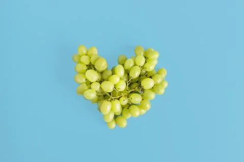 Fresh ripe grape falling in shape of heart in the air on blue background Stock Photos