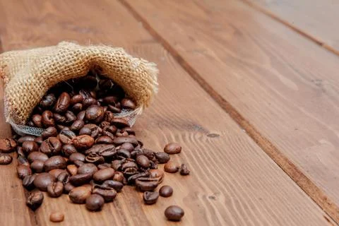 Fresh roasted coffee beans falling out the sack on the wooden surface. Brown  Stock Photos