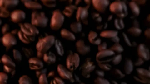 Fresh roasted dark coffee beans exploding in slow motion toward the camera lens Stock Footage 147555211