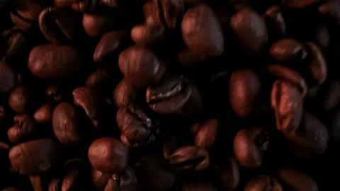 Fresh roasted dark coffee beans exploding in slow motion toward the camera lens Stock Footage 147556925