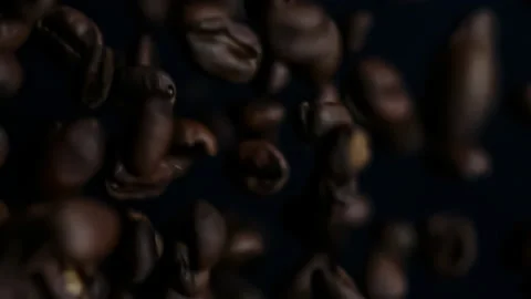 Fresh roasted dark coffee beans exploding in slow motion toward the camera lens Stock Footage 147677424