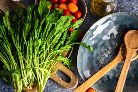 Fresh rocket, tomatoes and olive oil next to a plate with salad servers Stock Photos