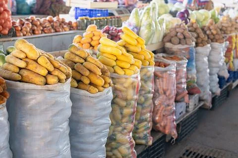 Fresh root vegetables in large sacks at bustling market stall. Yellow, orange Stock Photos