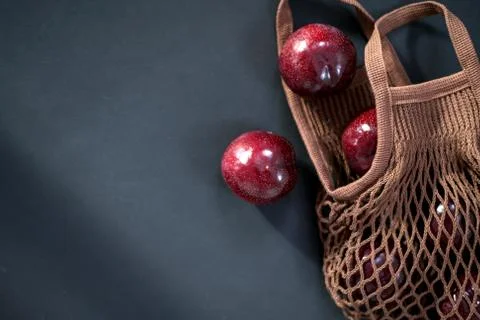 Fresh round purple plums, in a string bag , cotton grocery bag on a black Stock Photos