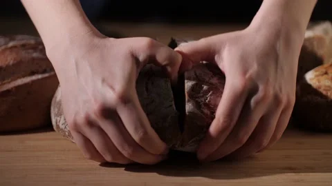 A fresh rustic bread loaf being ripped open by hand on wooden background. Stock Footage 145973543