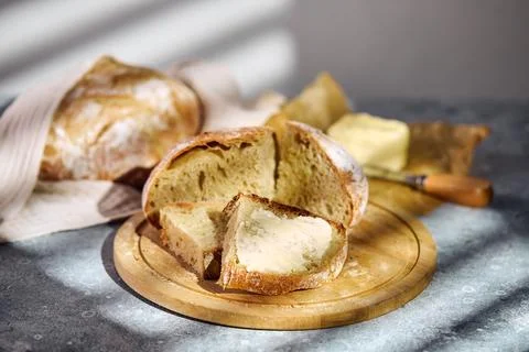 Fresh rustic bread slice with butter on wooden cutting board Stock Photos