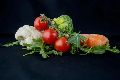 A fresh selection of vegetables on a black background. Juicy cherry tomatoe.. Stock Photos