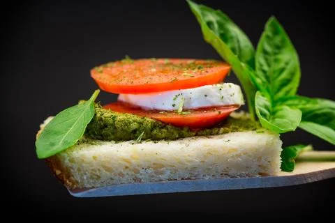 Fresh slice of bread with pesto sauce, mozzarella and tomato on a wooden sp.. Stock Photos