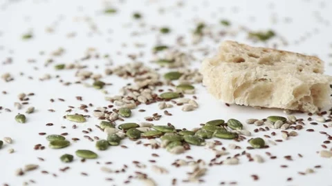 Fresh slice of sourdough bread dropping onto seeds on white surface slow motion Stock Footage 195999276