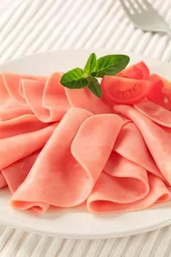 Fresh sliced ham with basil garnish on plate Stock Photos