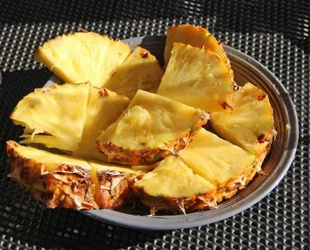 Fresh sliced pineapple chunks served on plate outdoors in sunlight Stock Photos