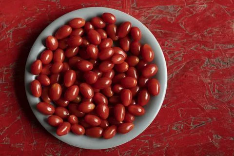 Fresh small cherry tomatoes on a grey plate and a red background 스톡 사진
