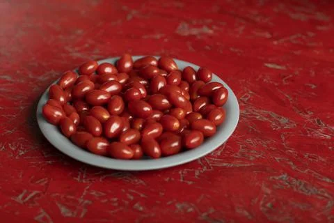 Fresh small cherry tomatoes on a grey plate and a red colored background 스톡 사진