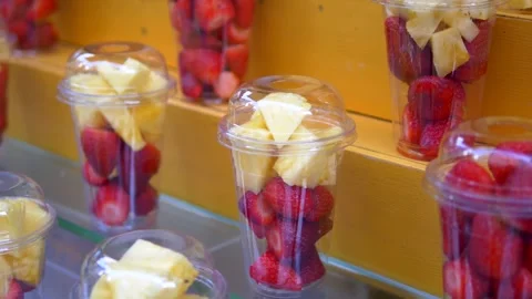 Fresh strawberries and pineapple chunks in plastic cups displayed on wooden.. Vídeos de archivo 333158544