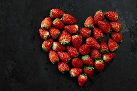 Fresh strawberries array heart shape on black background. Love concept Foto stock