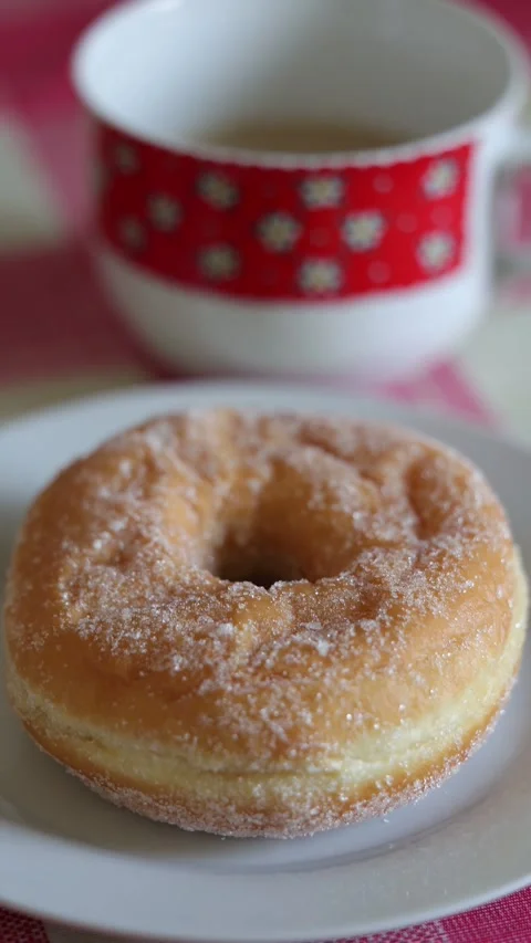 Fresh sugared donut on plate with coffee cup in background Stock Footage 346254589