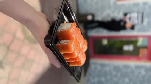 Fresh sushi rolls in plastic packaging on the palm of a girl on a sunny day at Stock Footage 243260398