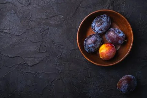 Fresh sweet plum fruits in brown wooden bowl, black textured background Stock Photos