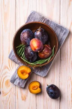 Fresh sweet plum fruits whole and sliced in brown wooden bowl with rosemary Stock Photos