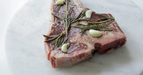 Fresh T-Bone or Porterhouse dry aged steak on marble cutting board. Garlic, oil Stock Footage 131437776