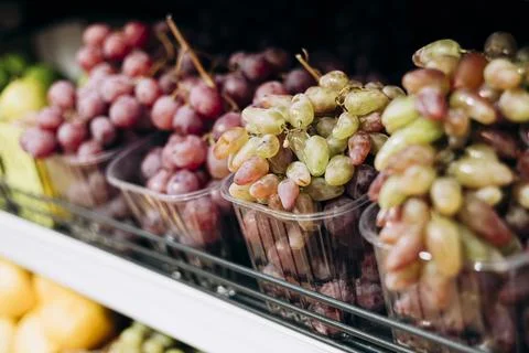 Fresh table grapes packed in plastic containers for sale at a market or store Stock Photos