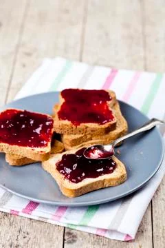 Fresh toasted cereal bread slices with homemade cherry jam and spoon on ceram Stock Photos