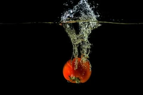 Fresh tomato dropped into water, isolated on dark background Stock Photos