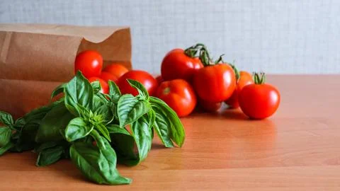 Fresh tomatoes and basil on a kitchen table with a brown paper bag nearby Stock Photos