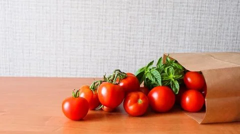 Fresh tomatoes and basil placed on a wooden table with brown paper bag on a Stock Photos