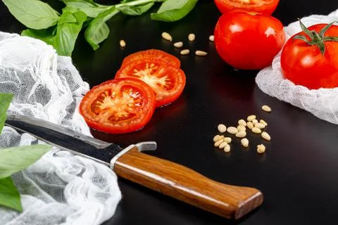 Fresh tomatoes with pine nuts, basil, knife and gauze on black background Stock Photos
